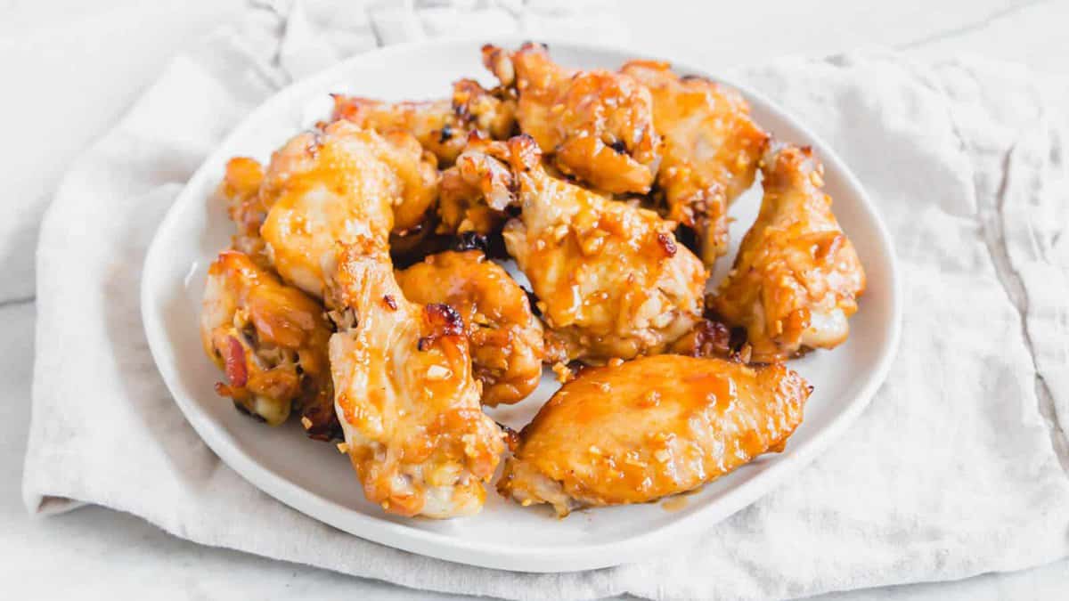 A white plate filled with baked chicken wings coated in a golden, glossy sauce, placed on a light cloth napkin.