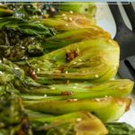 Halved bok choy roasted in the oven, garnished with sesame seeds and seasoning, arranged on a white plate.