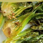 Close-up of roasted bok choy halves topped with sesame seeds and chopped garlic, accompanied by text reading "roasted bok choy" and "easy side dish.