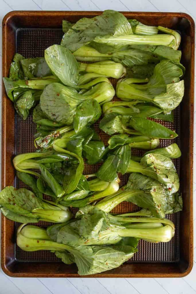 A baking tray filled with seasoned baby bok choy arranged in a single layer, ready for roasting.