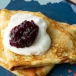 Two folded Swedish pancakes topped with whipped cream and a scoop of berry jam, served on a blue plate.