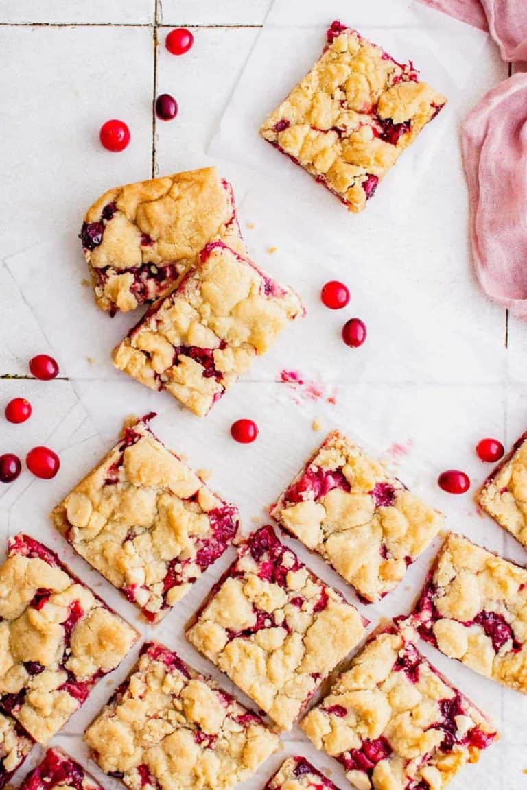Overhead view of cranberry crumb bars cut into squares, arranged on parchment paper with scattered whole cranberries.