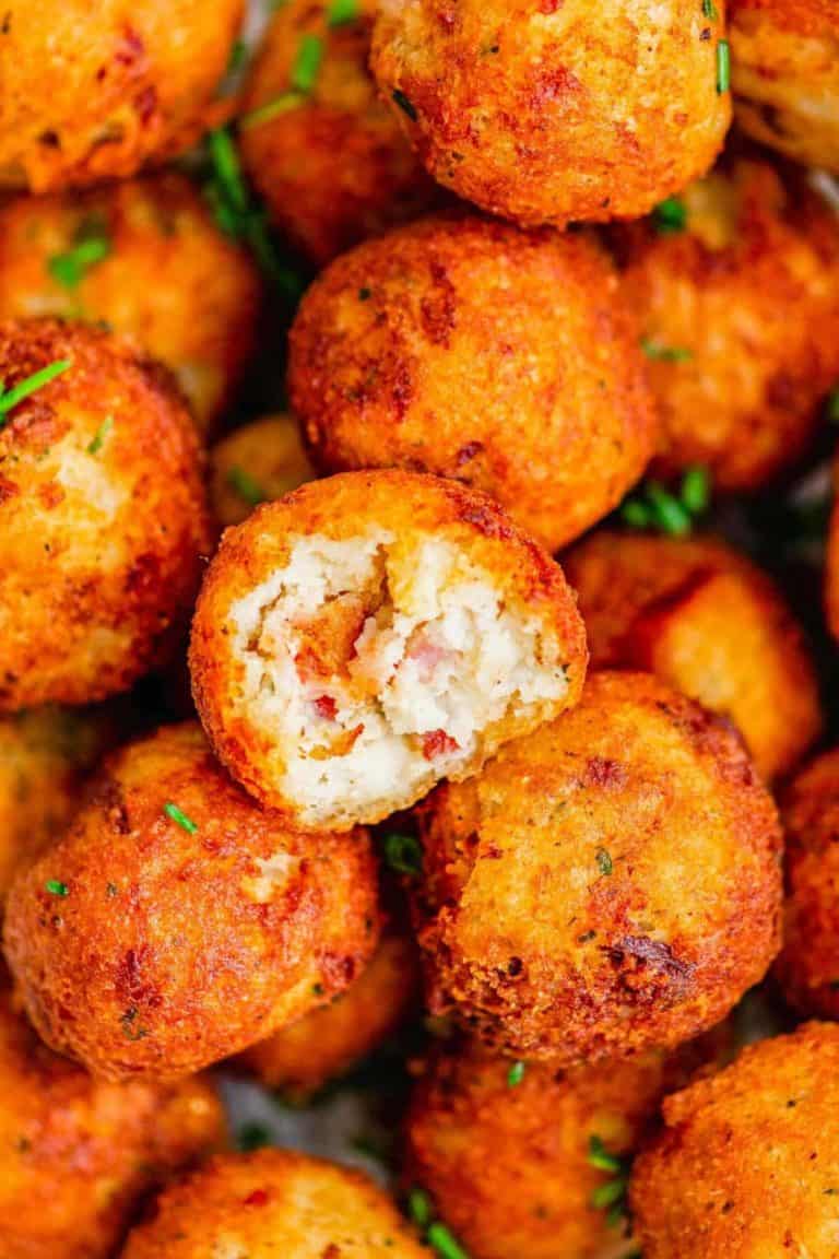 Close-up of golden-brown, crispy fried balls with a bite taken out of one, revealing a soft filling with small bits of bacon or ham inside.