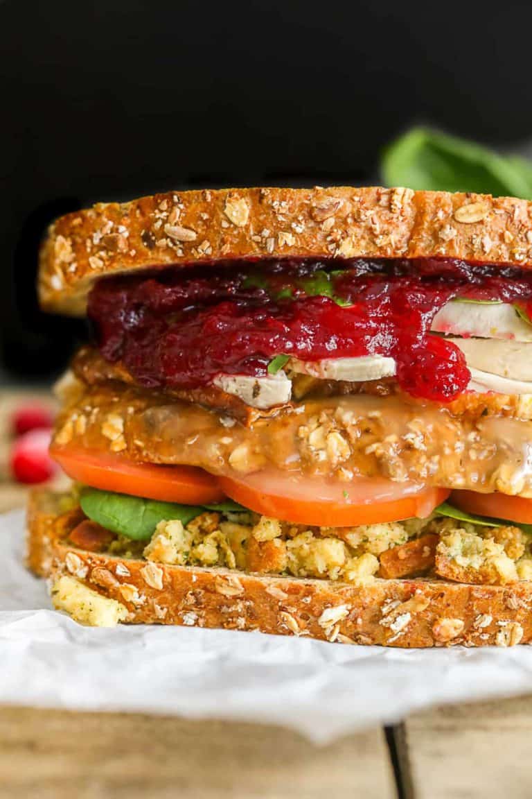 A close-up of a sandwich with whole grain bread, lettuce, tomato, stuffing, turkey slices, and cranberry sauce.