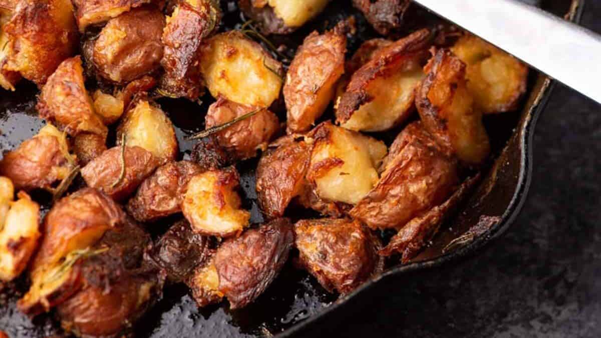Close-up of crispy roasted potato chunks with browned edges in a cast iron pan.