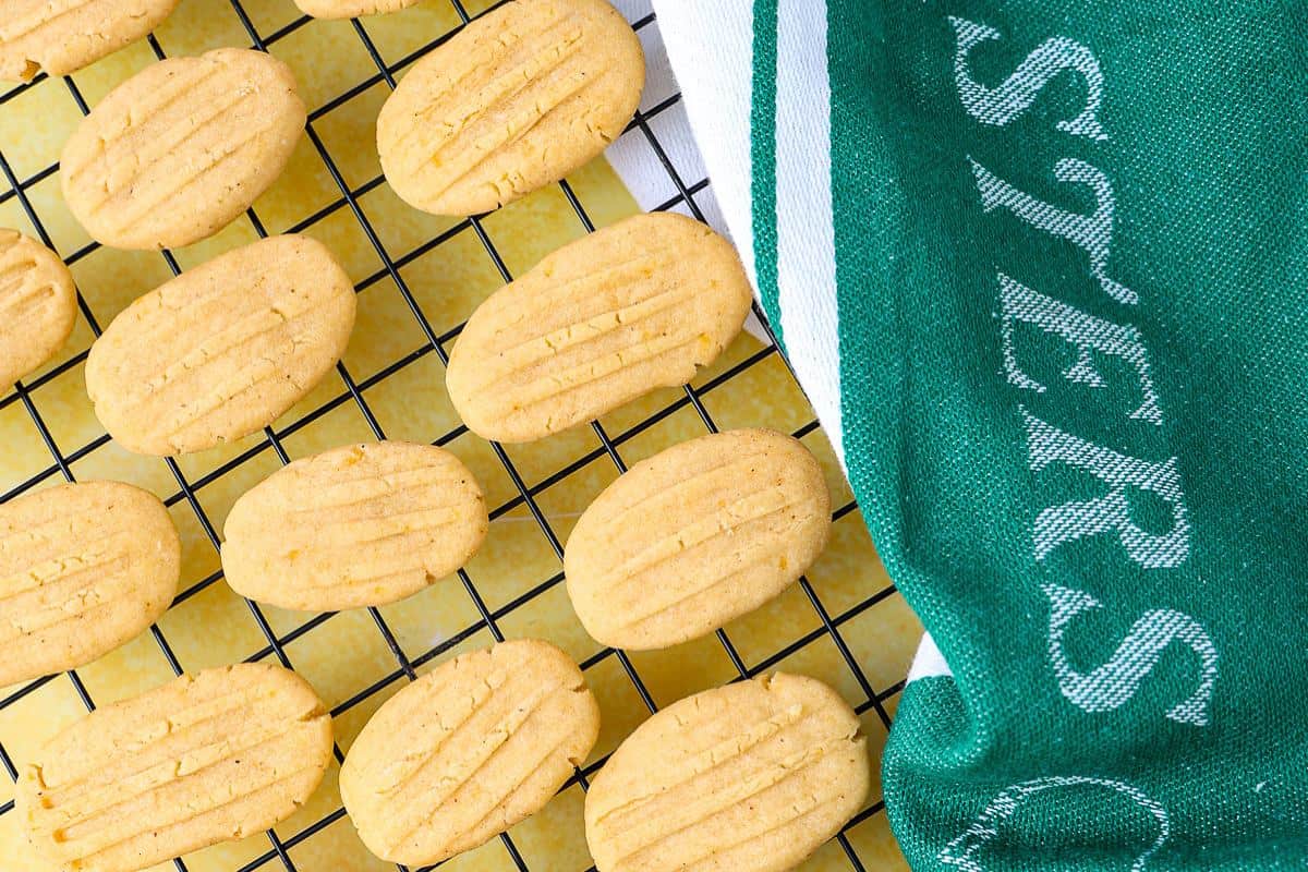 Oval-shaped cookies cool on a black wire rack next to a green and white towel.