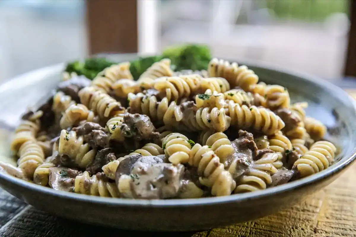 A plate of rotini pasta mixed with a creamy sauce, ground meat, and mushrooms, garnished with chopped herbs.