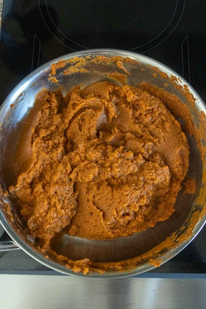 A metal pot containing a thick, smooth, brownish-orange paste sits on a black stovetop.