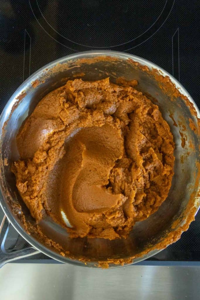 A saucepan filled with thick, brown pumpkin puree mixture sitting on a stovetop.