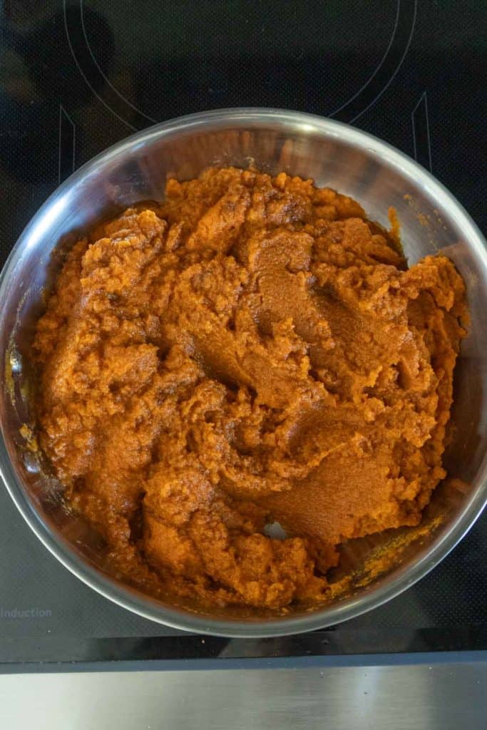 A stainless steel pan filled with a thick, orange-brown paste sits on a black stovetop.