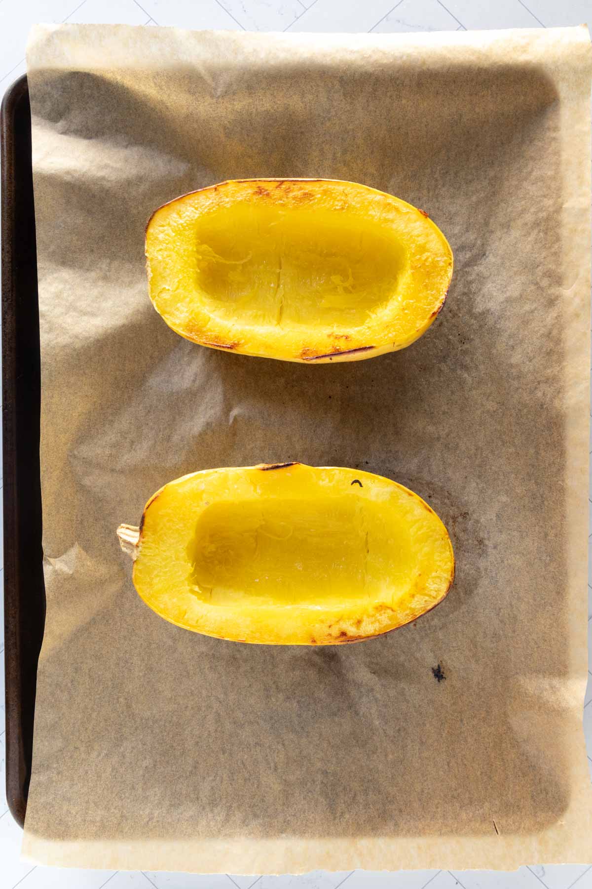 Two halves of roasted spaghetti squash placed cut side up on a parchment-lined baking sheet.