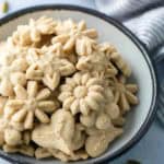 A bowl filled with assorted flower- and heart-shaped pressed cookies, with a striped cloth and whole spices nearby.