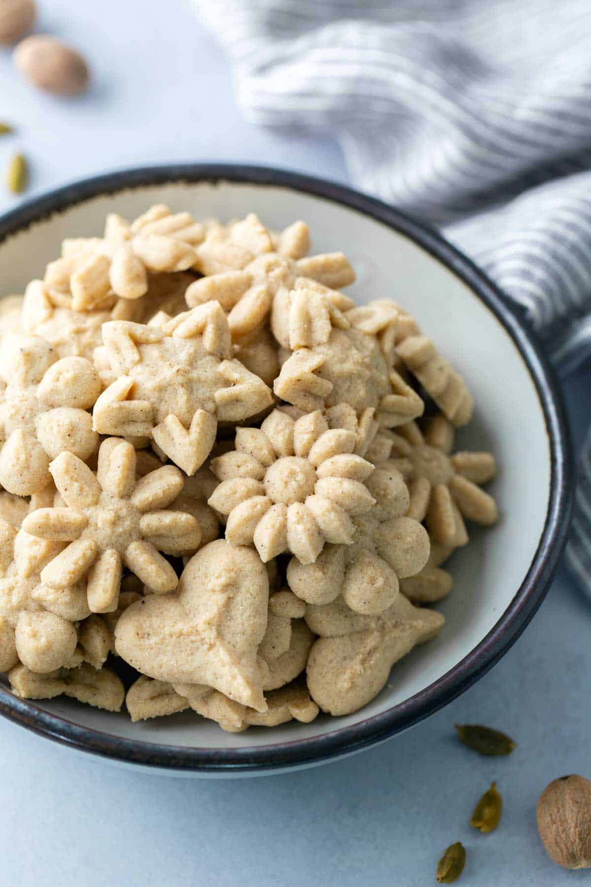 Chai Spritz Cookies for the 2014 #OXOGoodCookies campaign are a flavorful way to celebrate the season. A bowl filled with assorted flower- and heart-shaped pressed cookies, with a striped cloth and whole spices nearby.