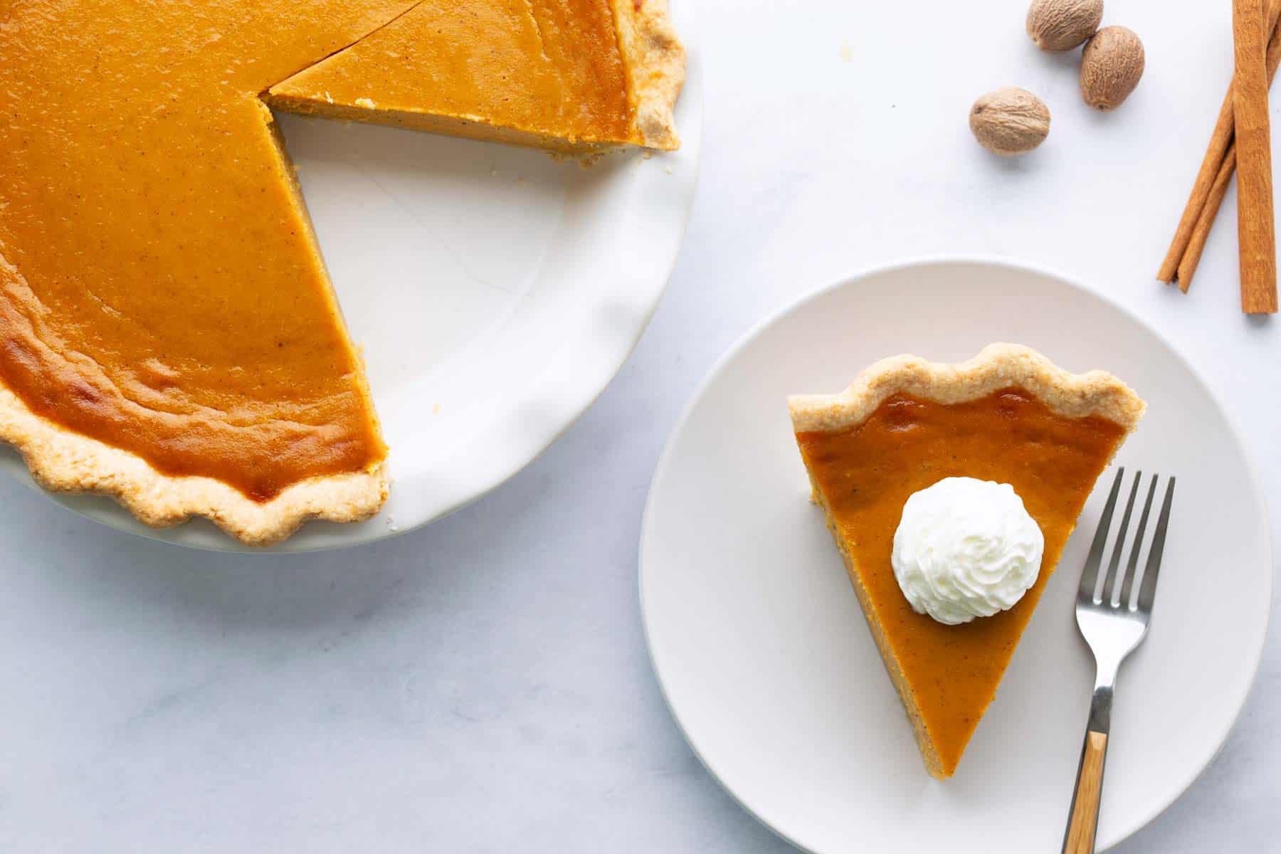 A slice of sweet potato pie with a dollop of whipped cream next to the whole pie.