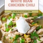 A bowl of white bean chicken chili topped with a dollop of sour cream, chopped green onions, and cilantro, with a spoon on the side. Text overlay reads "White Bean Chicken Chili.