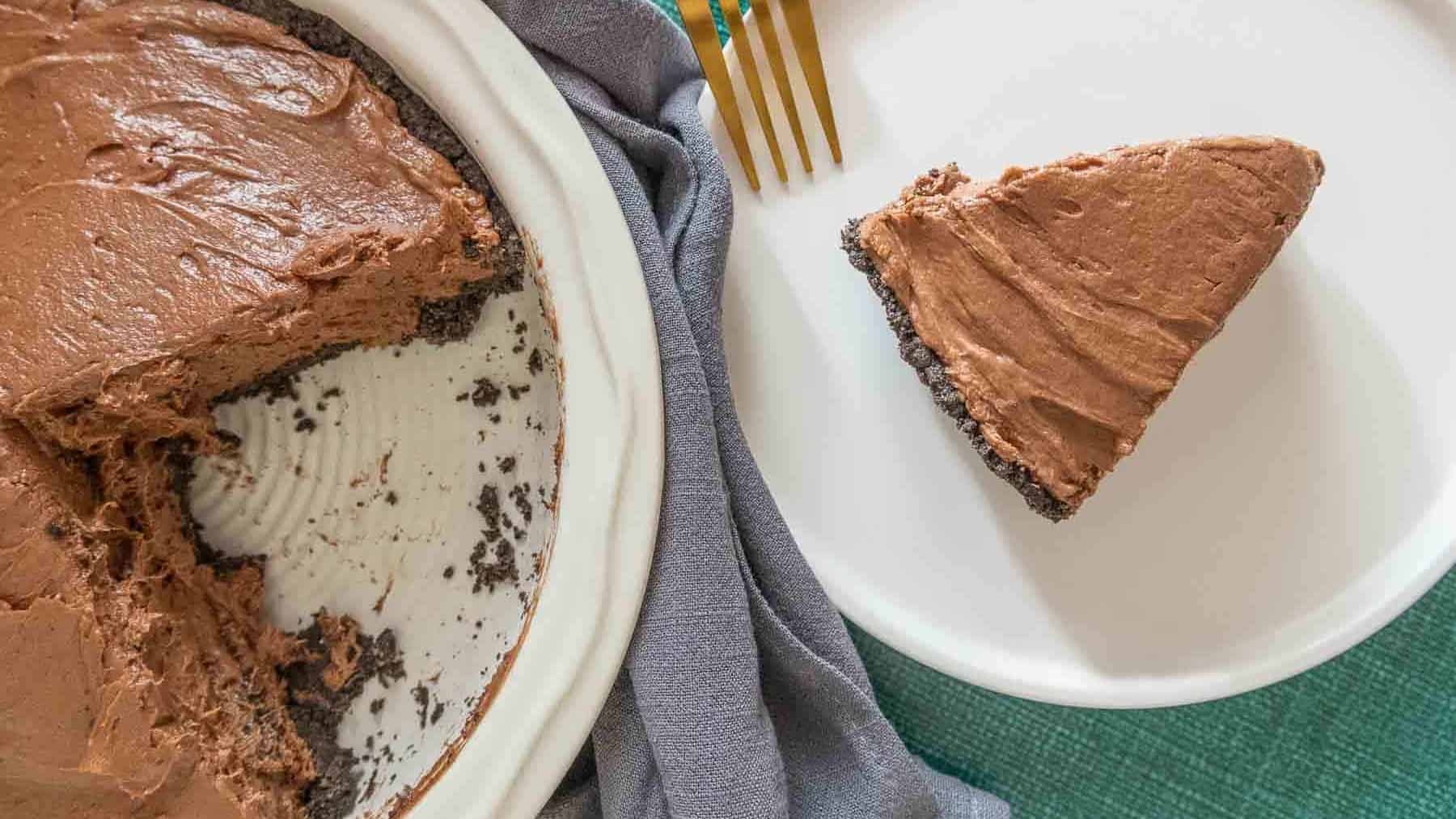 Slice of chocolate peanut butter pie on a plate with rest of pie nearby.