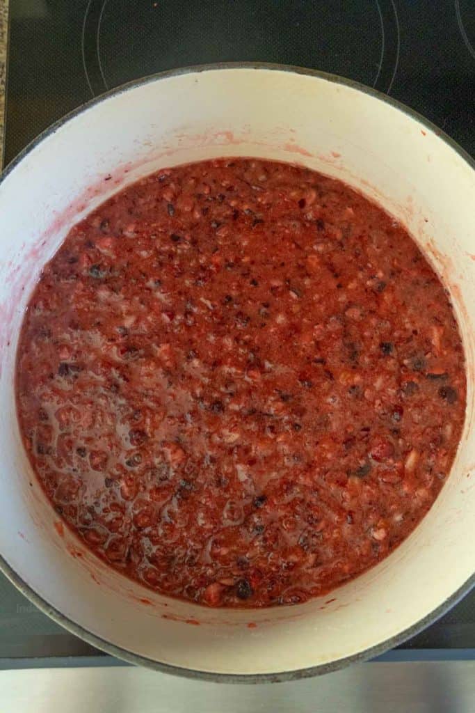 A pot of thick, chunky red fruit mixture cooking on a stovetop, likely cranberry sauce or jam.
