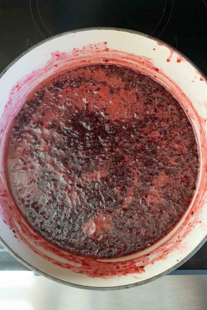 A pot filled with boiling berry mixture, likely being cooked down to make jam or preserves.