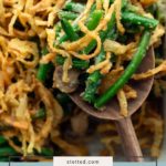 Close-up of green bean casserole topped with crispy fried onions, served on a wooden spoon. Text reads "fresh green bean casserole.