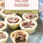 A tray of pecan tassies with one tassie in the front showing a bite taken out, revealing the pecan filling. Text overlay reads "Pecan Tassies. Get the recipe at stetted.com.