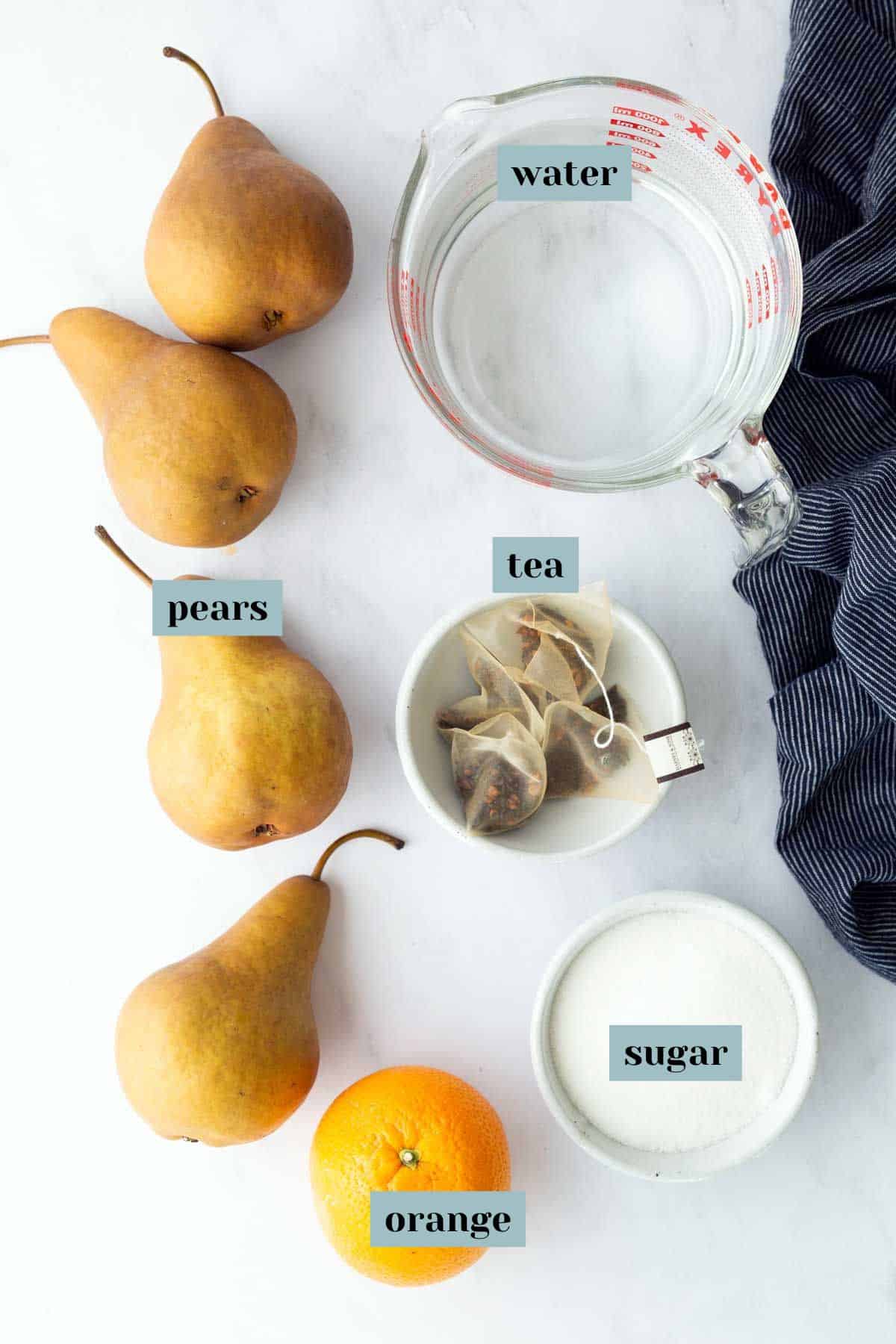 Four pears, an orange, a measuring cup of water, a small bowl of tea bags, and a bowl of sugar arranged on a white surface with labels for each ingredient.