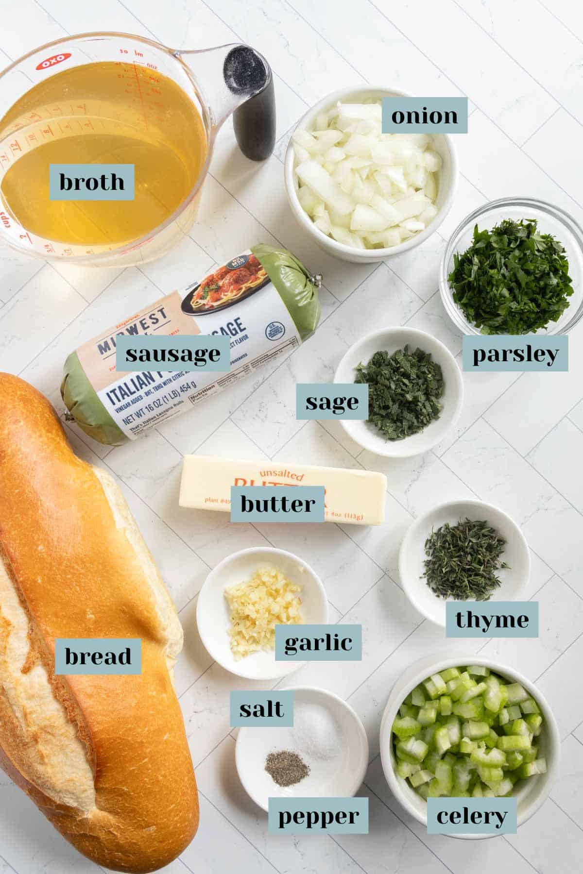 Top-down view of ingredients for stuffing: broth, Italian sausage, chopped onion, parsley, sage, thyme, celery, garlic, salt, pepper, butter, and a loaf of bread, all labeled.