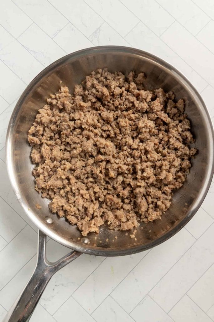 A stainless steel skillet filled with cooked and crumbled ground meat sits on a white tiled surface.