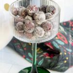A glass goblet filled with sugared cranberries sits on a patterned cloth, with "Sugared Cranberries" written at the top.