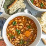 Two bowls of black-eyed pea soup with carrots and herbs, served with slices of bread on the side, placed on a patterned cloth.