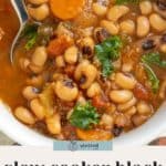 A bowl of slow cooker black-eyed pea soup with vegetables like carrots and greens, shown with a spoon.