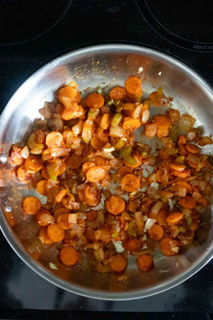 Sliced carrots, onions, and green peppers sautรฉing in a stainless steel pan on a stovetop.