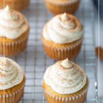 Four chai cupcakes with swirled frosting and a sprinkle of spice are arranged on a cooling rack. Text at the top reads "Chai Cupcakes.