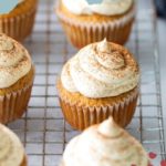 Cupcakes with swirled frosting and a dusting of spice on top, arranged on a wire cooling rack; text reads "Chai Cupcakes" at the top.