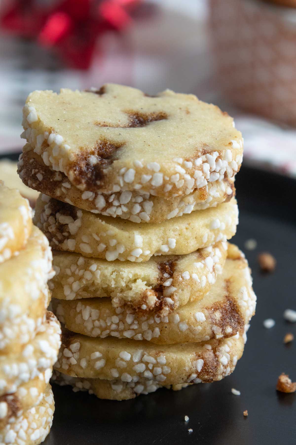 A stack of round, sugar-coated cookies with visible brown swirls sits on a black plate. Crumbs are scattered around.