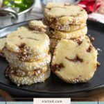 A plate of cinnamon roll cookies stacked and arranged on a black platter, with more cookies and baking ingredients in the background.