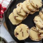A black plate with stacked cinnamon roll cookies, topped with pearl sugar, placed on a marble surface next to a red-striped towel and a red ribbon.