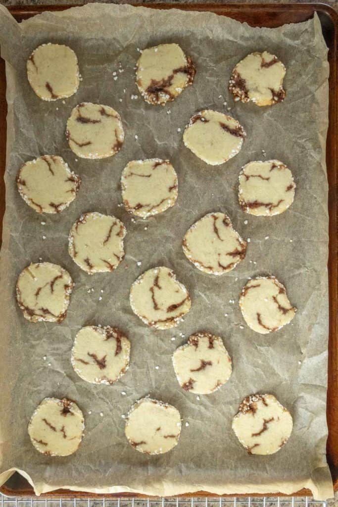 A baking tray lined with parchment paper holds 21 slices of marbled cookie dough arranged in rows, ready to be baked.