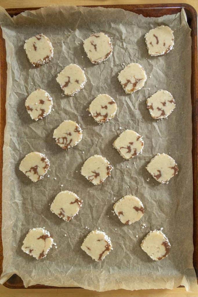 Sliced unbaked cookies with a marbled pattern are arranged in rows on a parchment-lined baking sheet.