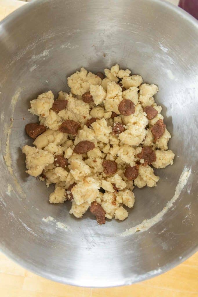 A metal mixing bowl containing a mixture of light and dark cookie dough crumbles.