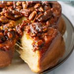 Close-up of pecan sticky buns on a plate, with one section pulled away to show the soft interior and caramelized pecan topping.