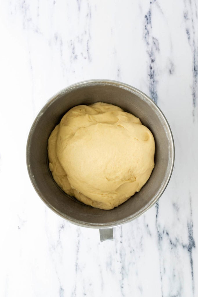 A mixing bowl filled with risen dough sits on a white marble surface.