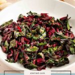 A white bowl filled with cooked beet greens and stems, garnished with lemon zest, sits on a light-colored surface.