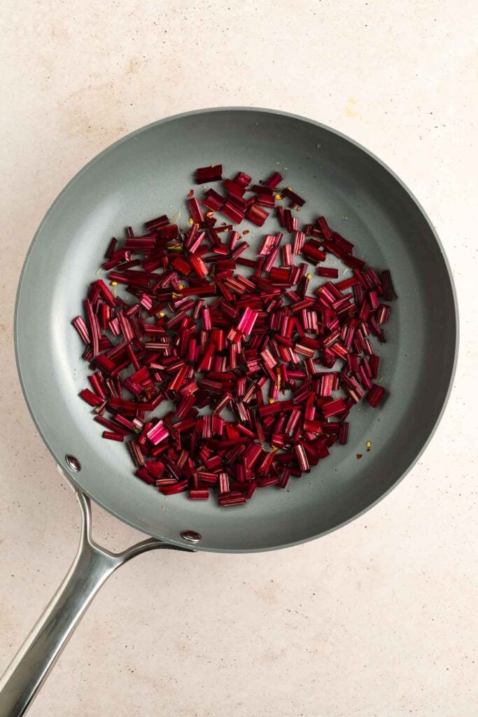 A frying pan containing chopped red vegetable stems, likely Swiss chard stems, on a light-colored countertop.