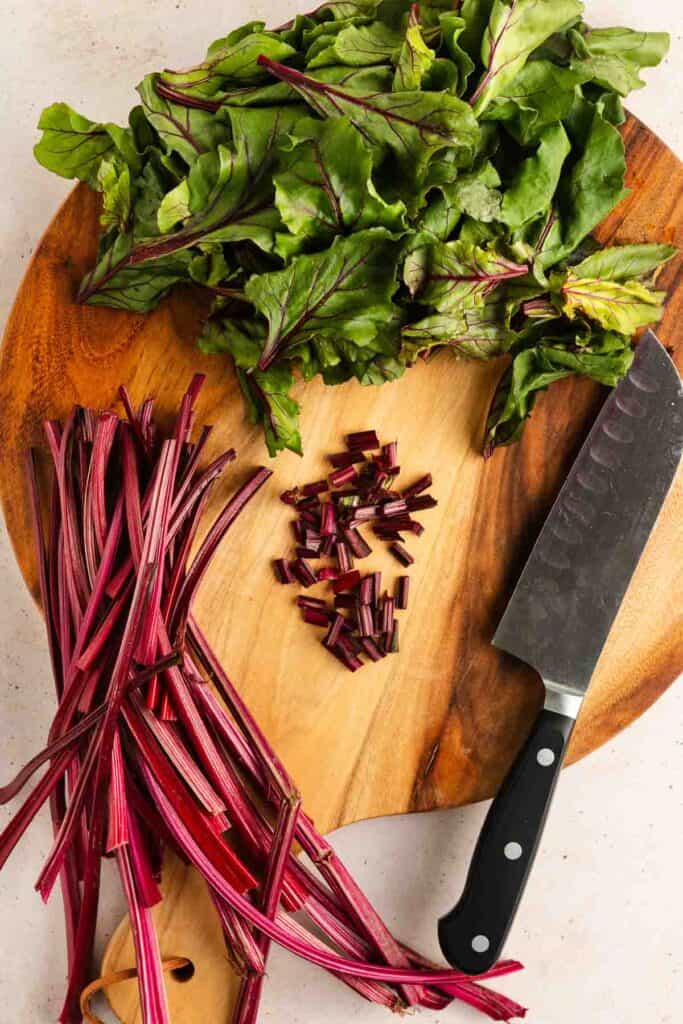 Chopped beet greens, stems, and a chef's knife are arranged on a wooden cutting board.