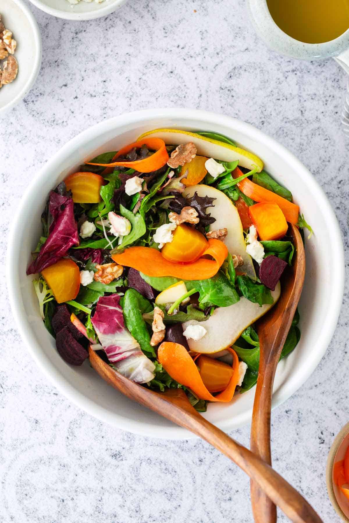 Beet Salad - Roasted Beet Salad has a light citrus vinaigrette. A bowl of mixed greens salad with sliced carrots, beets, pears, walnuts, and cheese, served with wooden salad servers.