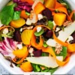 A bowl of roasted beet salad with mixed greens, sliced pears, carrot ribbons, walnuts, and goat cheese crumbles.