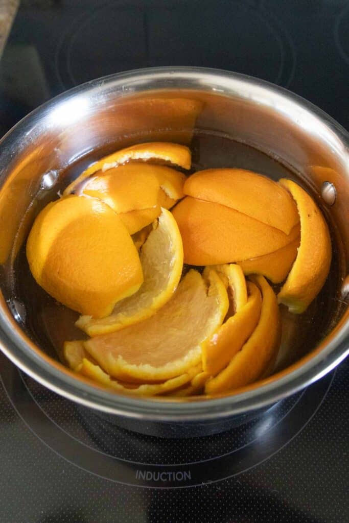 A stainless steel pot filled with orange peels submerged in water sits on an induction stovetop.