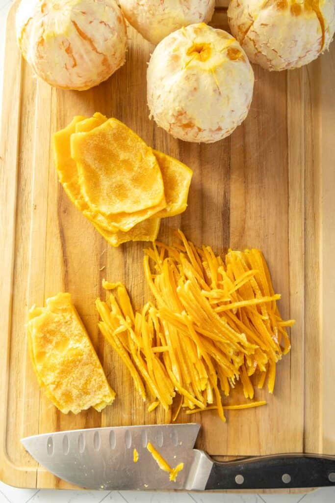 A cutting board with peeled papayas, sliced papaya skin, julienned papaya, and a knife.