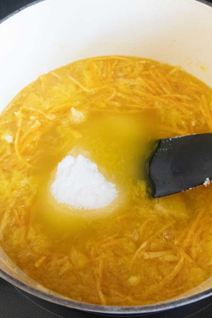 A pot of yellow soup or stew with shredded ingredients, a mound of salt or white seasoning in the center, and a black spatula resting in the mixture.