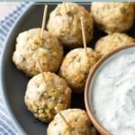 A plate of Greek turkey meatballs with toothpicks, served next to a bowl of creamy white dipping sauce.